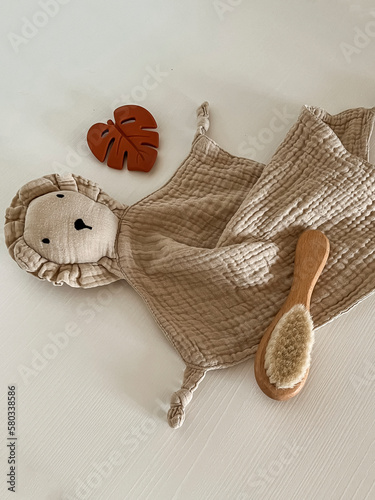 a children's toy-a handkerchief in the form of a beige lion, a rodent leaf of a monster and a wooden hair brush on a light white background. view from above. flatley. copy space