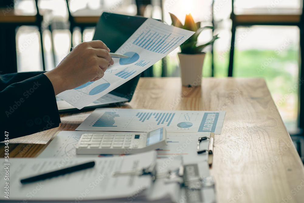 Fototapeta premium Business finance manager holding financial graph document to analyze company monthly expenses while sitting in the office Holding chart and graph paper in hand with laptop on table