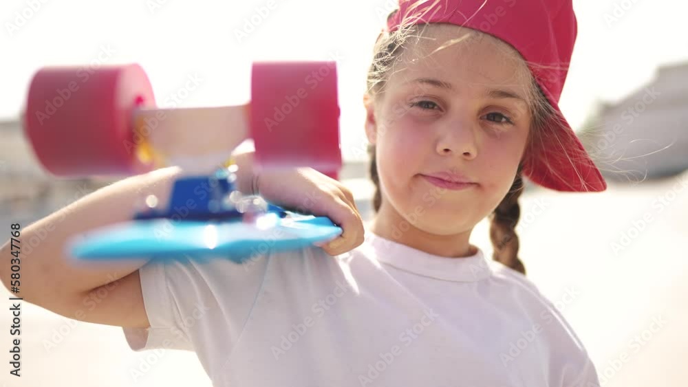 child with a skateboard. girl in a red cap with a skateboard on the playground portrait