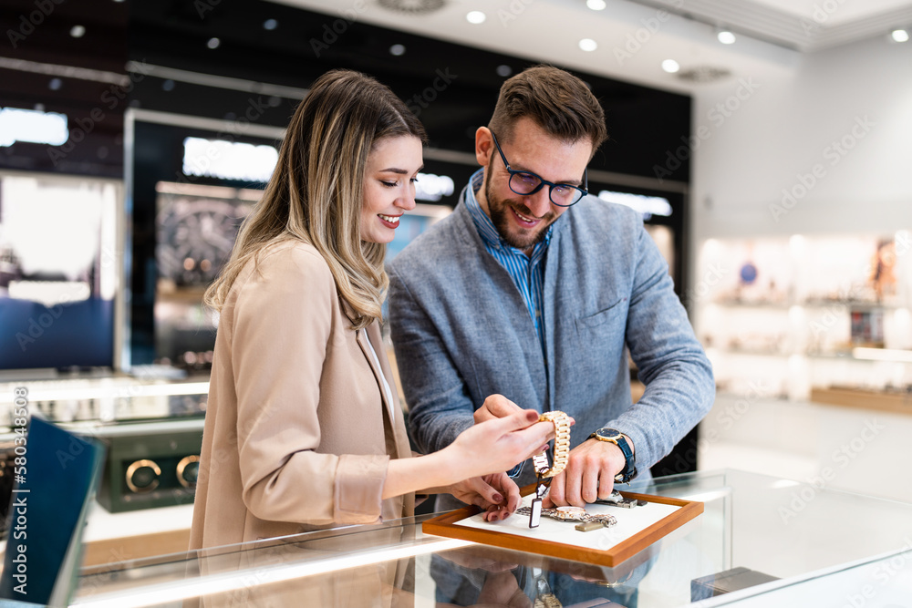 Elegant middle age businessman choosing and buying his new expensive watch. Beautiful young female seller helps him to make good decision. Fashion style and elegance concept. - obrazy, fototapety, plakaty 
