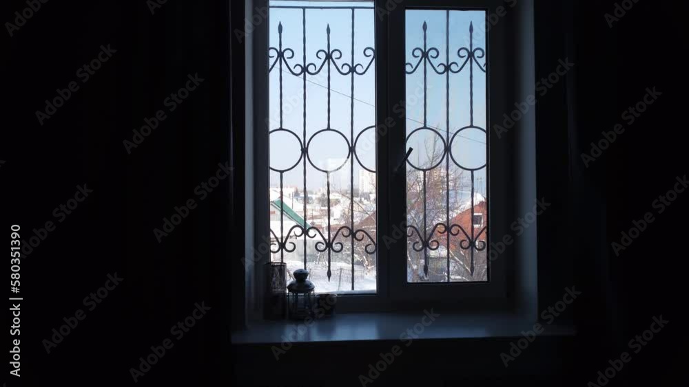 View of the old courtyard from the window of a private house. Snow outside the window. The camera zooms in on the window through the dark room.