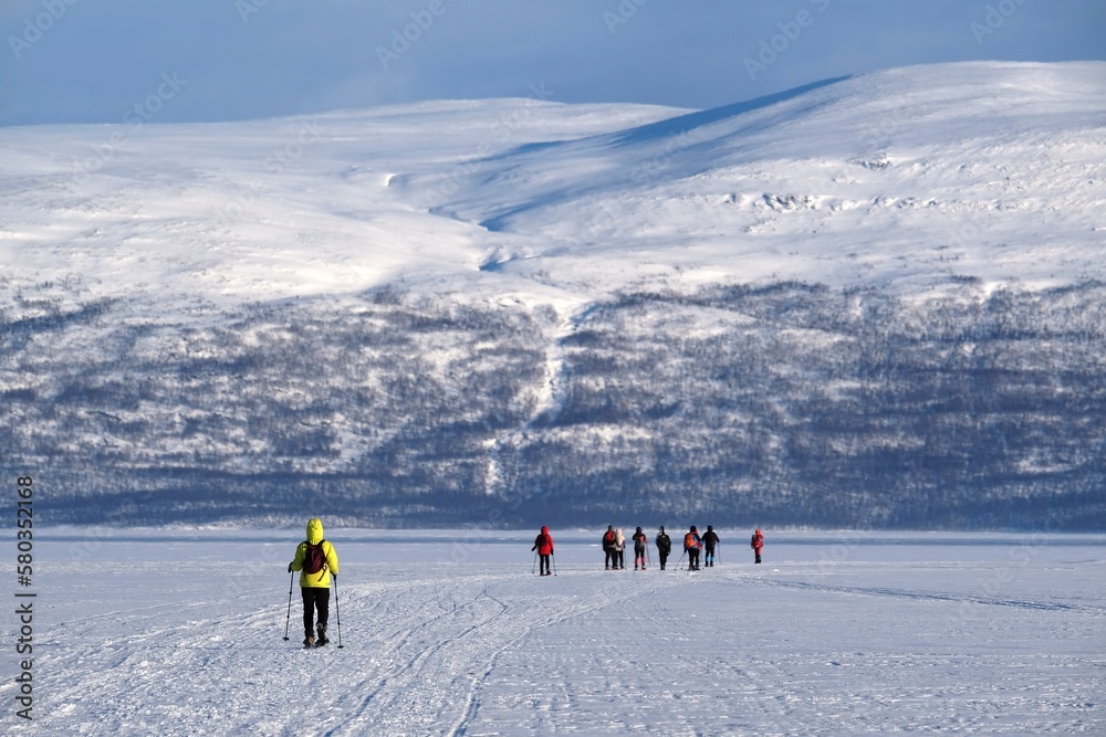 Silhouettes of tourists on snowshoes on lake Torneträsk (Tornestrask) around Abisko National Park (Abisko nationalpark) in winter scenery. Sweden, Arctic Circle, Swedish Lapland