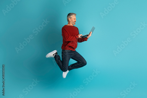 Happy middle aged man digital nomad jumping with laptop