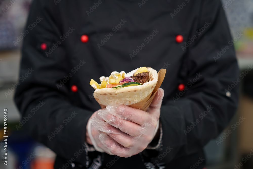 Cook holds gyros wrapped in pita bread. Traditional Greek fast food dish cooked with natural ingredients - grilled chicken meat, fries and white tzatziki sauce