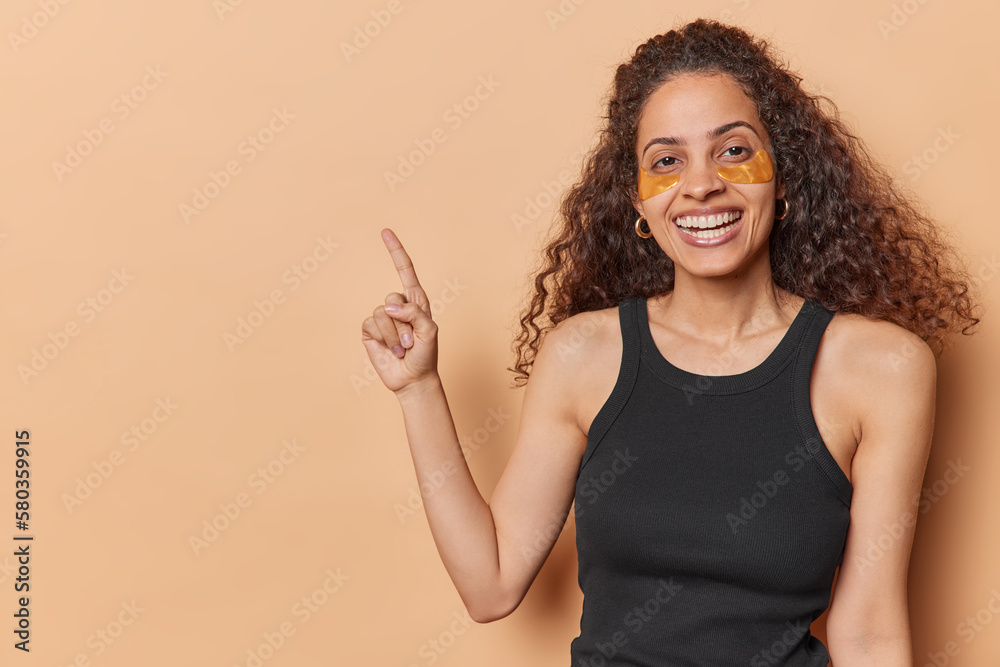 Happy curly haired woman applies collagen beauty patches under eyes has