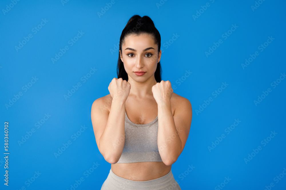 Obraz premium Athletic brunette woman standing in defence position on blue