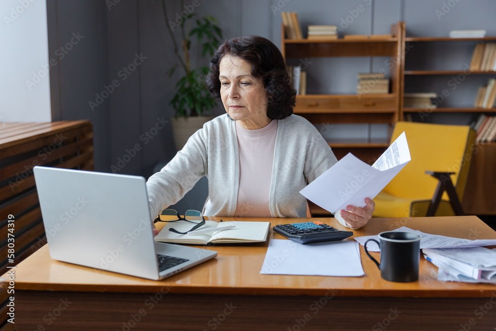 Middle aged senior woman sit with laptop and paper document, Pensive older mature lady reading paper bill pay online at home managing bank finances calculating taxes planning loan debt pension payment Middle aged senior woman sit with laptop and paper document, Pensive older mature lady reading paper bill pay online at home managing bank finances calculating taxes planning loan debt pension payment