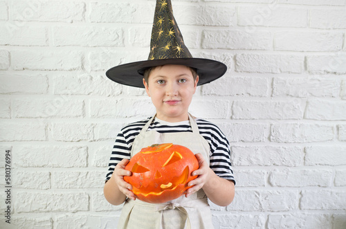 A little boy is holding a carving pumpkin in white background.