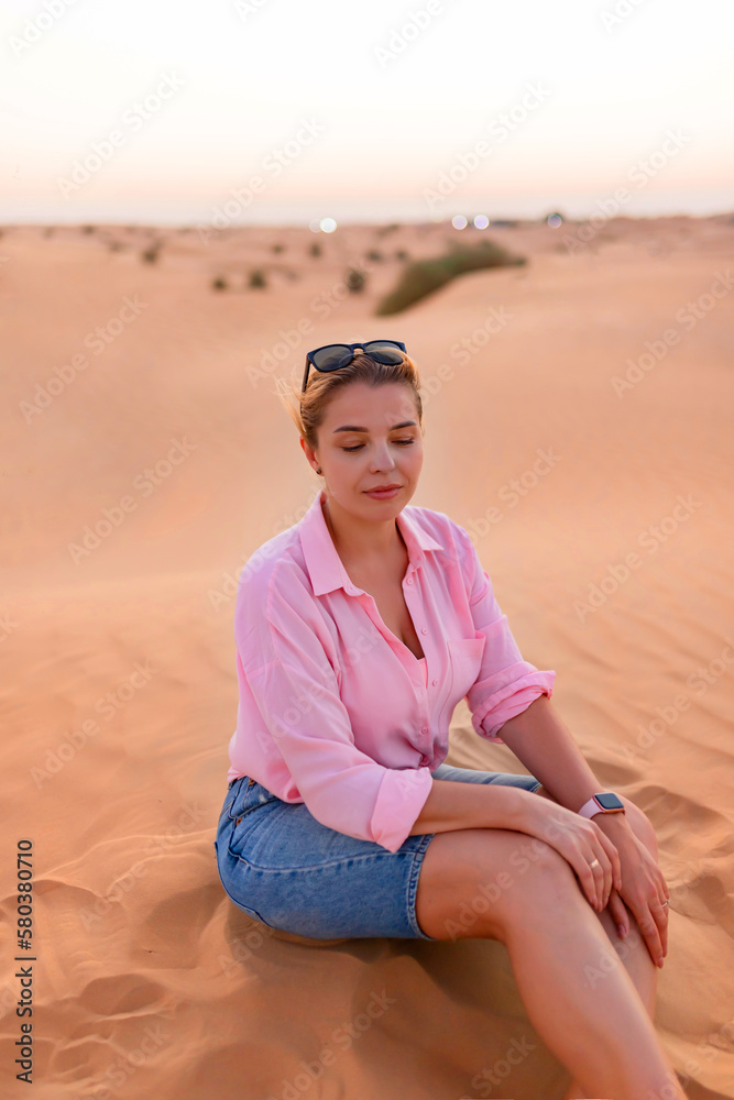 European attractive woman sitting on the crest of a dune in desert