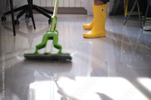 Фотография determined young boy in yellow boots is working hard to restore his home after a flood