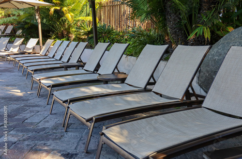 A row of launch chairs by swimming pool. Poolside sitting area for sunbathing and relaxing.