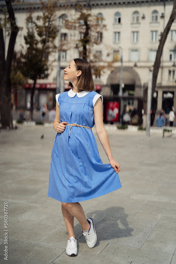 Portrait happy pregnant woman chilling and having fun while walking in the city in a midi blue vintage dress. Happiness all around