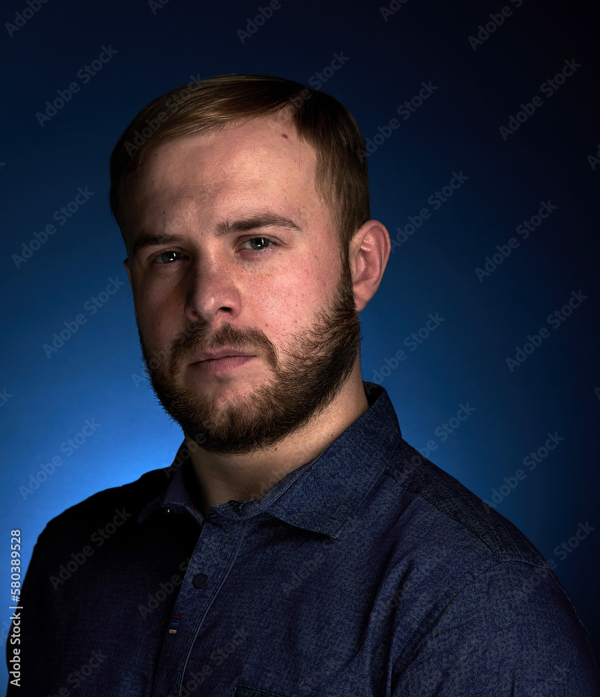 Portrait of a young confident blonde in a dark shirt, with a beard on a dark background