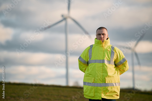 A male engineer man is standing in a wind turbine field with a beautiful sky background. Concept of sustainable future.