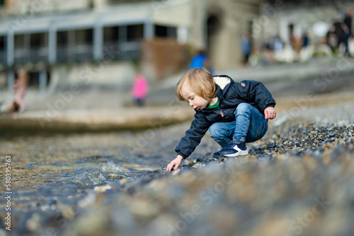 Cute toddler boy playing with pebbles in the harbor of Varenna, one of the most picturesque towns on the shore of Lake Como. Varenna, Italy.