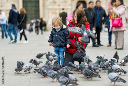 Young mother and her toddler son feeding the pigeons on the Cathedral Square or Piazza del Duomo in the center of Milan, Italy.