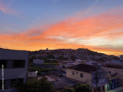 Dawn over a small town, with blue and orange skies, with a street in the foreground and a hill full of houses in the background. © Keila