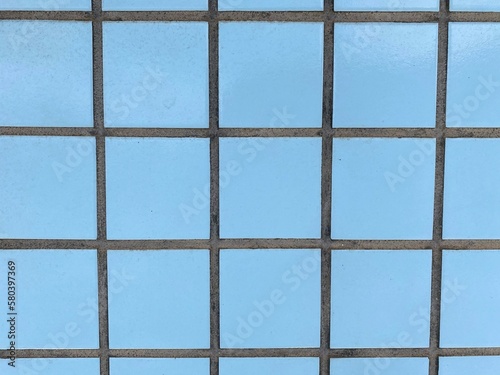 wall of light blue tiles, in small squares, with darkened grout.