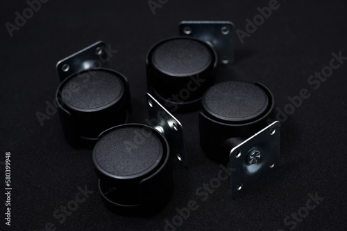 Black plastic furniture rollers on a black background.
