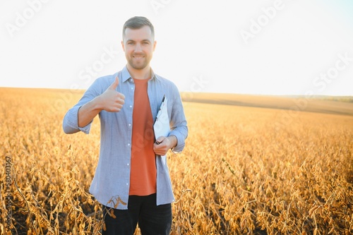 agronomist or farmer examining crop of soybeans field.