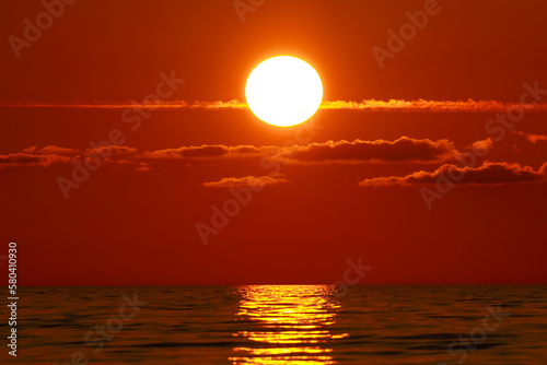 Big red sun setting over ocean and sun reflection trail on water surface