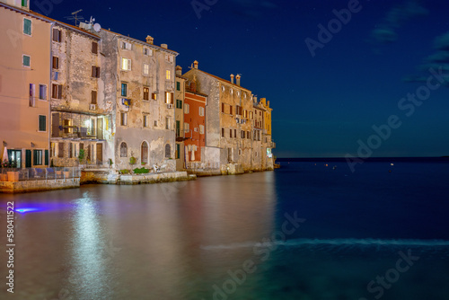 Old multi storey houses in various colors and different shuttered windows right next to sea bay at night in Rovinj old town, Croatia
