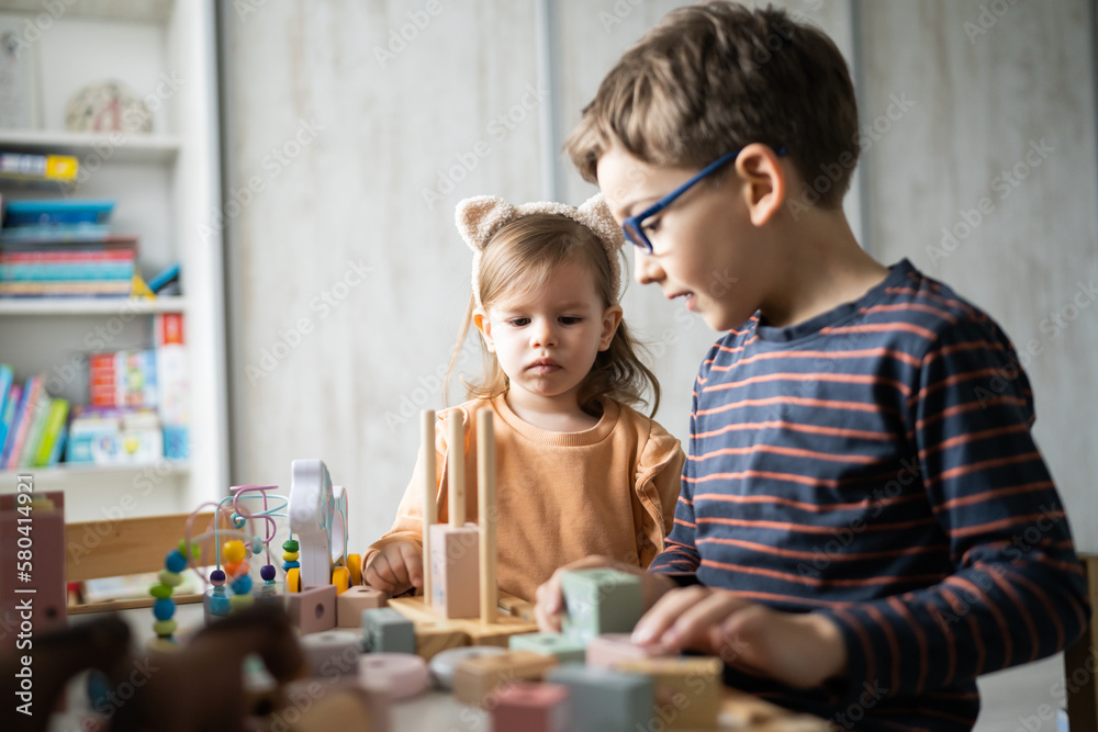 Fototapeta premium Two children brother and sister sitting and playing at home with wooden toys in playroom, modern family, early child development, learning and play concept