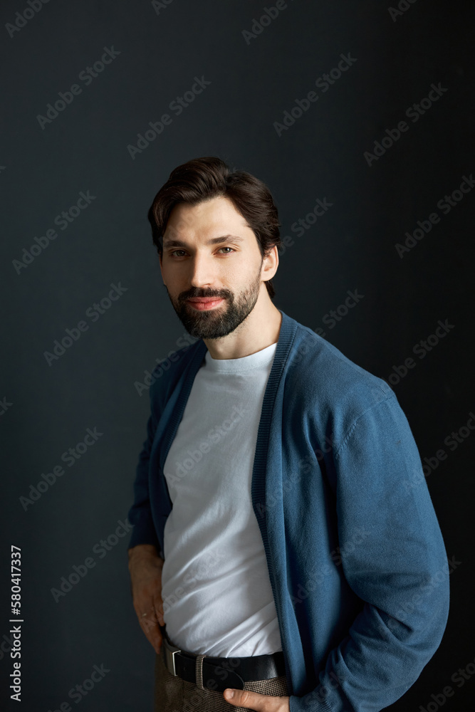 Attractive bearded successful small business owner standing against black background in casual clothes with hands in pockets, feeling happy, proud and confident, looking at camera with candid smile Attractive bearded successful small business owner standing against black background in casual clothes with hands in pockets, feeling happy, proud and confident, looking at camera with candid smile