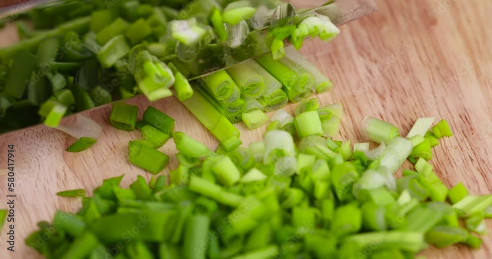 Green onion is sliced on a wooden chopping board, fresh green onion feathers during chopping Green onion is sliced on a wooden chopping board, fresh green onion feathers during chopping