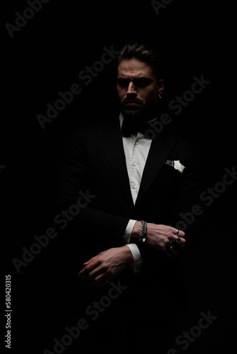 bearded young man in elegant tux holding arms in fashion pose