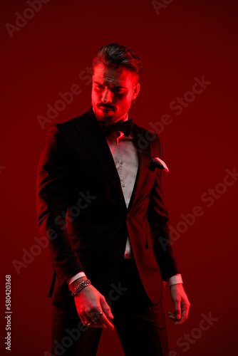 sexy elegant groom wearing black tuxedo and looking to side