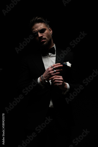 Fotografia stylish unshaved groom in tuxedo touching fingers and posing