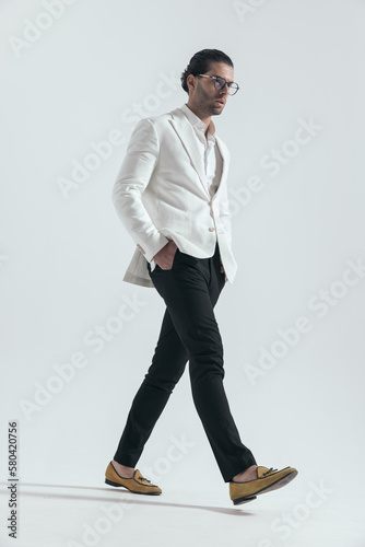 side view of cool fashion man walking with hands in pockets photo