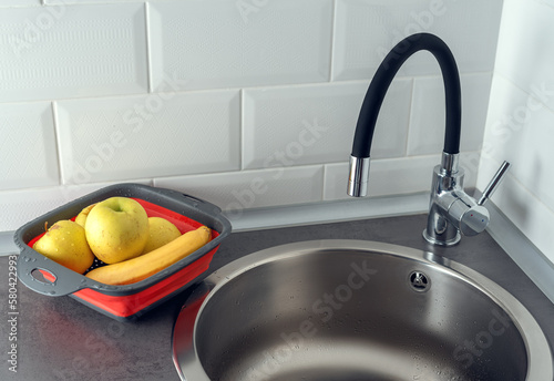Fruits in a colander, sink and water faucet in the kitchen. Fruits washing.