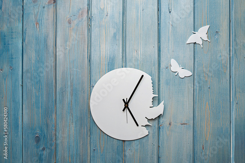 unusual white clock with black hands without numbers on a blue wooden wall with flying butterflies