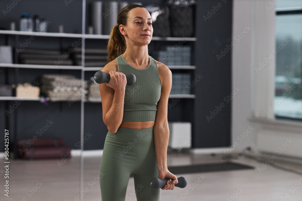 Young woman in sportswear exercising with dumbbells during her sport training in gym Young woman in sportswear exercising with dumbbells during her sport training in gym