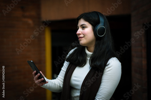 Girl listening to music in the city. Woman enjoying good music with her phone in hand. Smiling woman with headphones looking into the distance