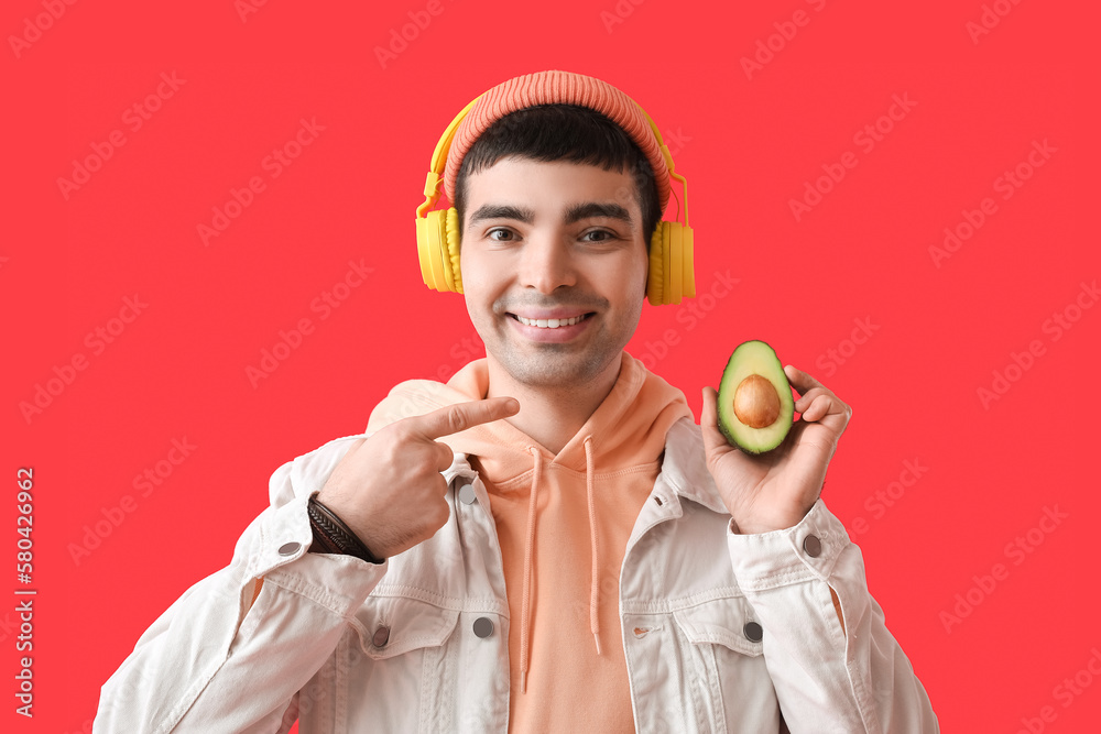 Young man in headphones pointing at avocado on red background Young man in headphones pointing at avocado on red background