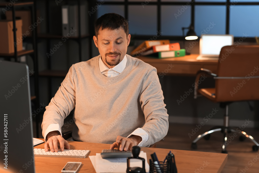 Male accountant working with computer and calculator in office at night Male accountant working with computer and calculator in office at night