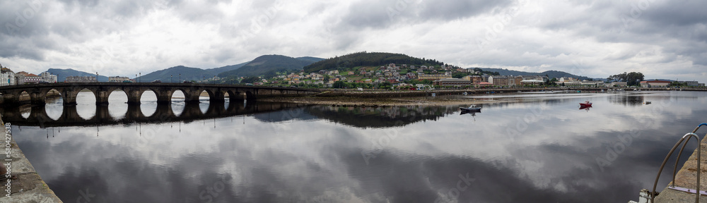 Vista panorámica de la ria de Vicedo en Lugo con vistas del viejo puente y nubes reflejadas en el agua del río, en Galicia, verano de 2021