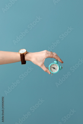 Woman with wristwatch and small alarm clock on blue background