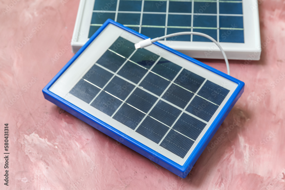 Portable solar panels with cable on pink grunge background