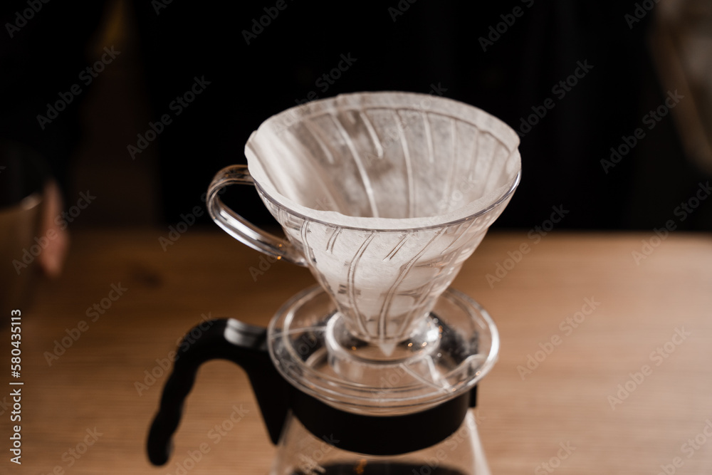 Pour over filter with ground coffee in the funnel in focus. Drip filter coffee brewing. Pour over alternative method of pouring water over roasted and ground coffee beans contained in filter.