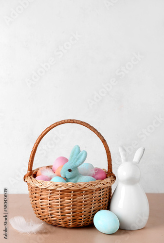 Basket with Easter eggs and bunnies on beige table against white background