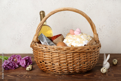 Basket with Easter eggs  cake and bottle of wine on wooden table against grey background