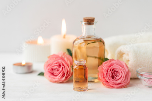 Aromatherapy. Concept of pure organic essential rose oil. Elixir with plant based floral or herbal ingredients. Pink flowers extract. Spa atmosphere with candle, towel. White background