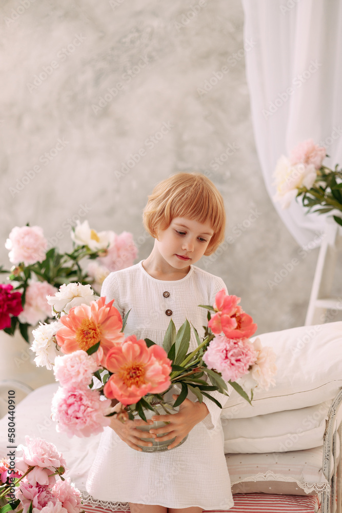Child Blond 6-7 years old in a white dress holds a large bouquet of pale pink flowers in her hand. The concept of congratulations on March 8, International Women's Day. Child Blond 6-7 years old in a white dress holds a large bouquet of pale pink flowers in her hand. The concept of congratulations on March 8, International Women's Day.