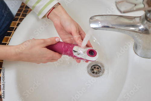 young woman washes a sex toy in the sink at home. photo