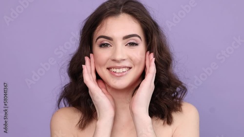 Beautiful brunette woman straightens her long curly hair and smiles, looking at the camera, touching her hairstyle. The concept of natural beauty, cosmetological procedures, the effect of makeup.