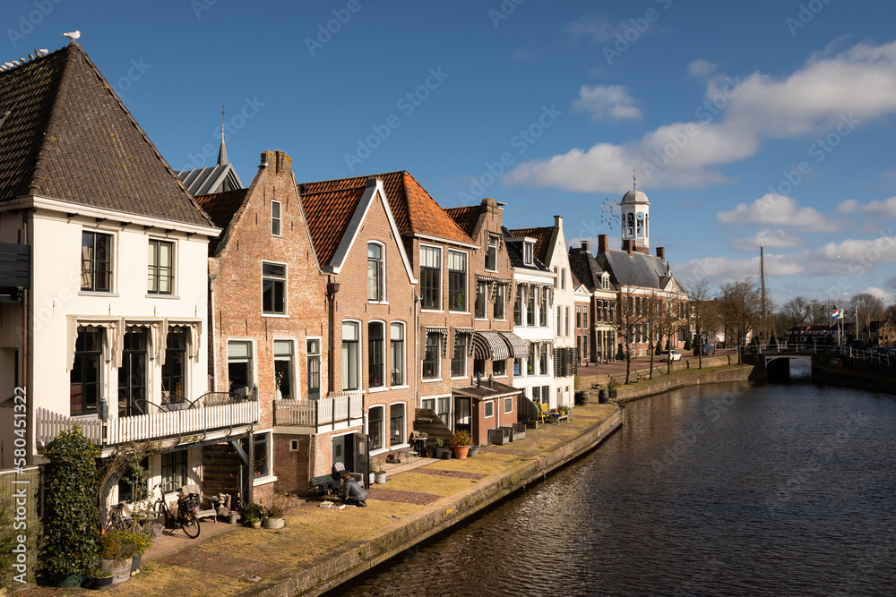 waterside residential houses on the edge of the river kleindiep waterway in Dokkum, Friesland, Netherlands Holland. old town hall  in town centre with bridge on pleasant sunny day